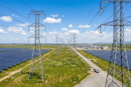 Aerial view of a large AI data center campus beside high-voltage transmission lines and power substation