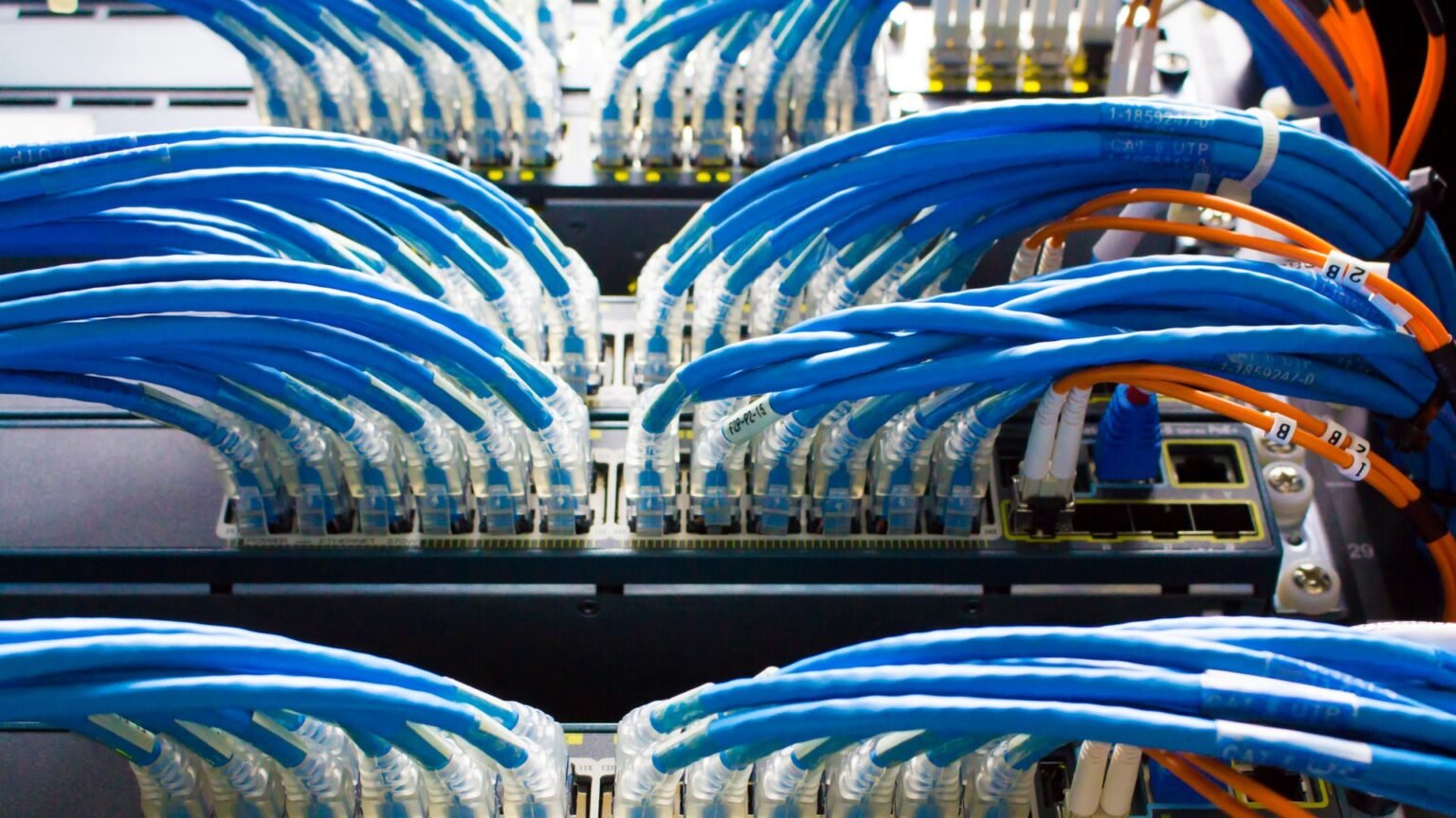 Rows of AI data center switches with dense fiber-optic cabling forming the back-end network fabric of a GPU cluster